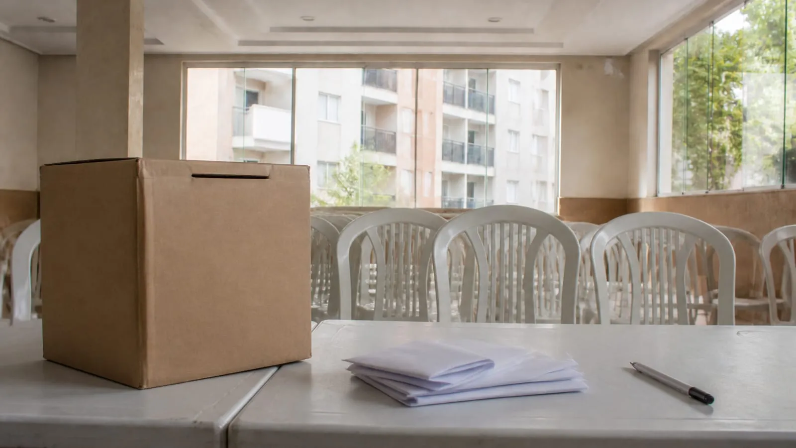 Urna de papelão e cédulas dobradas sobre uma mesa de assembleia