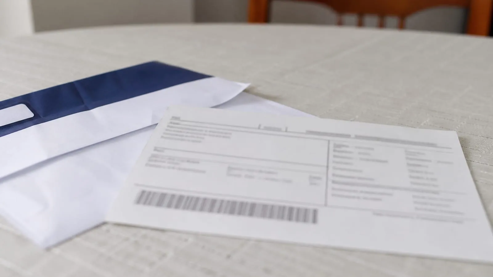 Boleto e envelope bancário sobre uma mesa de jantar, com números fora de foco